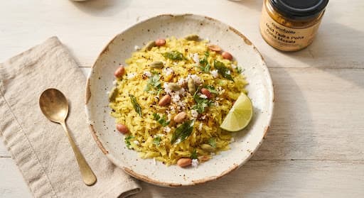 Thin golden Basmati poha flakes on a handmade ceramic plate with cardamom pods